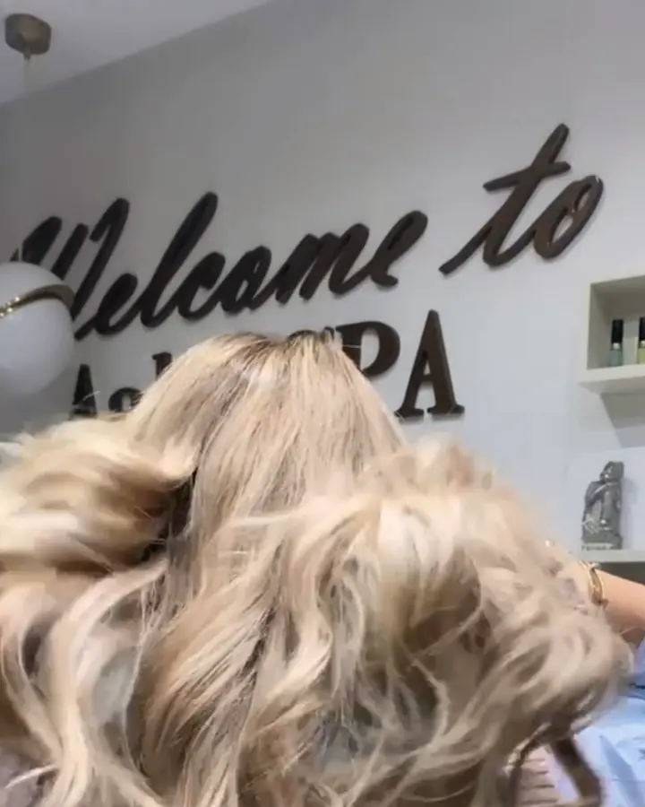 Cheveux blonds ondulés devant le mur Welcome to Aahd SPA