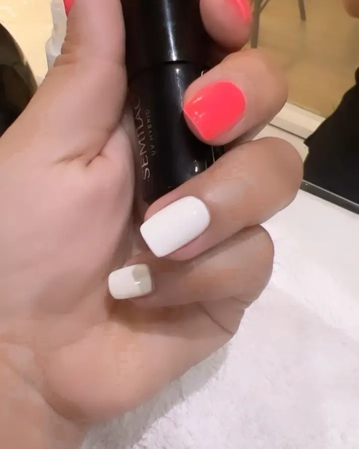 Ongles blancs et corail, main tenant un flacon de vernis